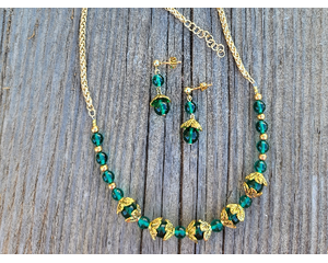 Emerald and gold jewelry set. Necklace has beaded focal point at the front with chains on both sides. Post earrings lay in the center.